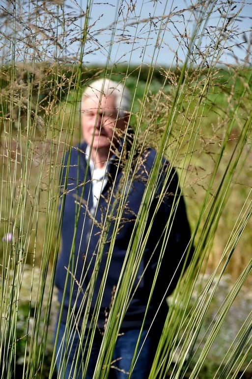 Piet Oudolf bij Plantwerk Piet Oudolf in een tuinomgeving, gefotografeerd achter siergrassen